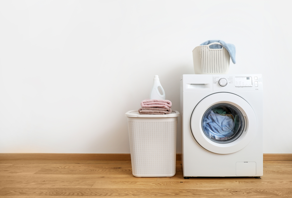 Waschmaschine, Waschkorb und Waschmittel vor weißer Wand