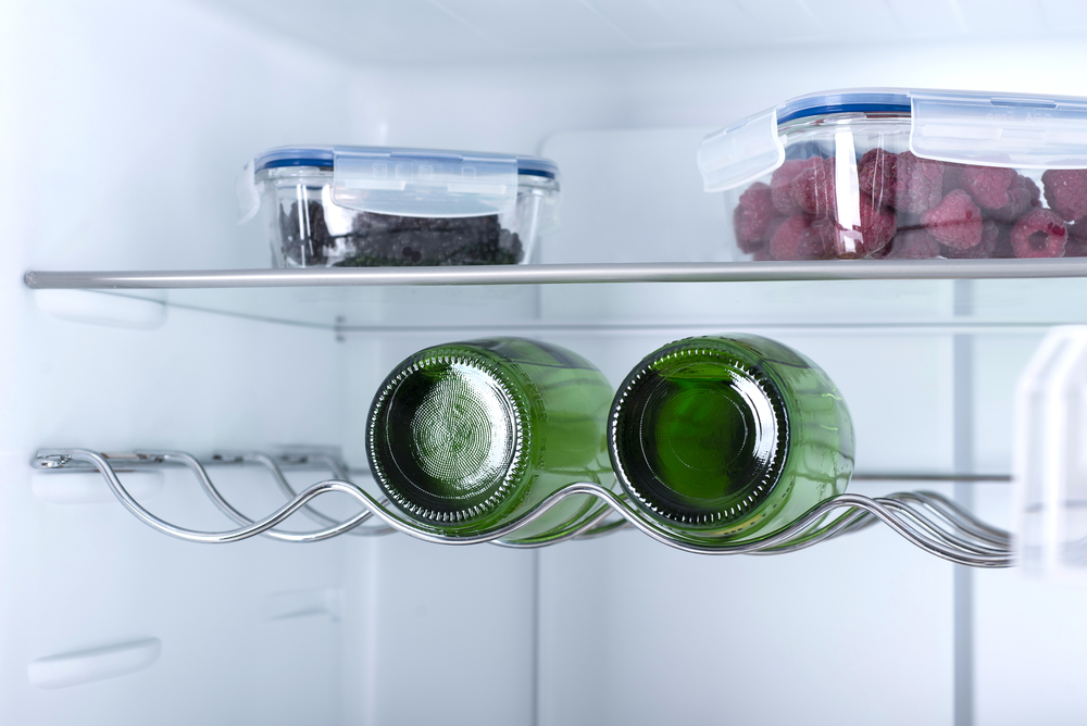 Offener Kühlschrank mit frischen Früchten und zwei braunen Flaschen