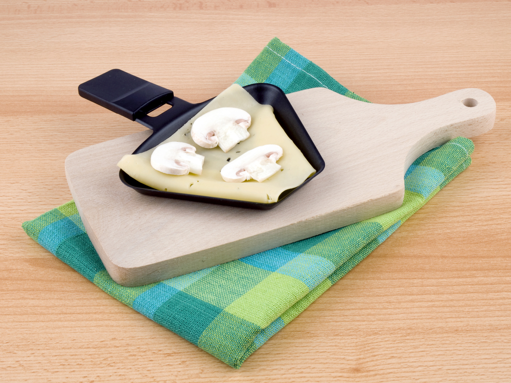 Raclette Pfanne mit Käse und Plizen auf einem gefalteten Handtuch