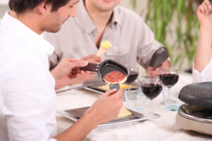 Seitenansicht eines jungen Mannes, der den Inhalt eines Raclette Pfännchens auf den Teller gibt.