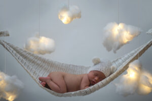 Kleines Baby schlafen in einer Hängematte, dahinter sind Wolken zu sehen