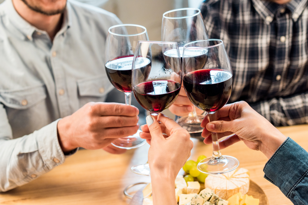 Vier mit Rotwein gefüllte Weingläser, mit denen angestoßen wird