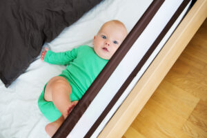 Baby liegt in einem Bett, das durch ein Geländer gesichert ist.
