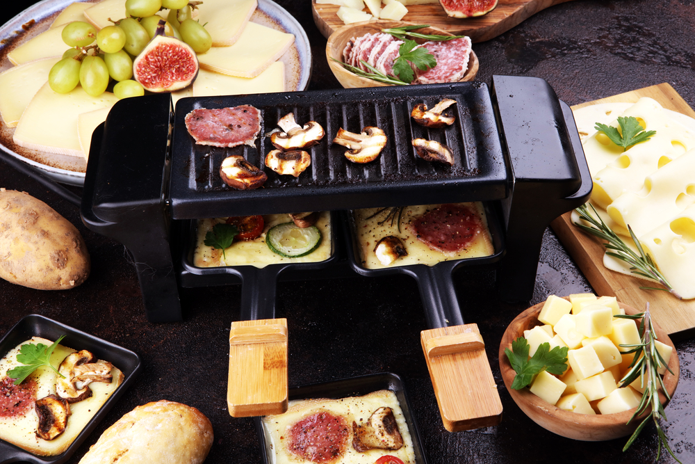 Ansicht eines Raclette Grills, in dem verschiedene Pfännchen mit Zutaten zubereitet werden.