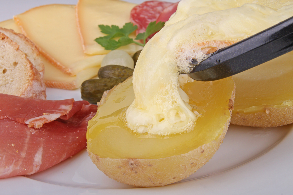 Geschmolzener Raclette Käse, der aus der Raclette-Pfanne auf eine Kartoffel gegossen wird